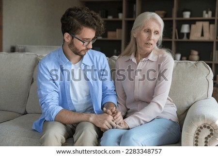 Loving adult son comforting worried concerned senior mother, sitting on couch, holding hand of elder mom, giving support, compassion, empathy, going through crisis, stress, bad news Royalty-Free Stock Photo #2283348757