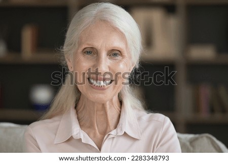Happy positive retired elderly lady home head shot portrait. Cheerful senior woman looking at camera with toothy smile, posing indoors. Video call screen view