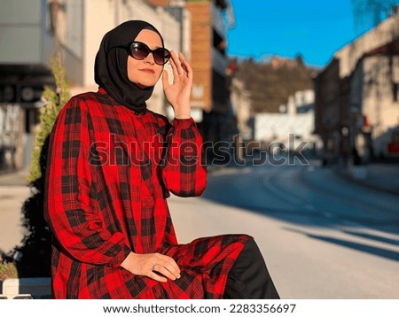 A young Muslim woman in a hijab is sitting on a bench in the city. High quality photo