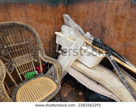 An old litter box piled on top of a rolled up rug amongst other items in a dumpster.