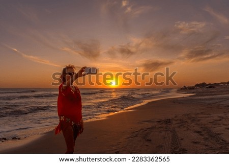 Senior woman taking a selfie with a mobile phone at the beach during the sunset. Summer, vacation, technology concept.