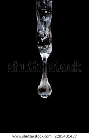 close up, macro of water drop forming and falling from single isolated icicle in front of dark background Royalty-Free Stock Photo #2283401459
