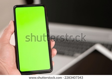 Horizontal view of cell phone with green chroma key in the screen with a laptop and tablet device in background and copy space