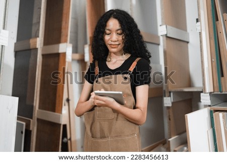 Happy teenager carpenter African American woman use tablet computer working with wood sheet at wood factory	