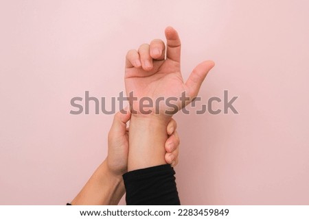 Close-up of woman's hand holding her painful wrist from Arthritis or Carpal Tunnel Syndrome (CST) isolated on pink background. Health care concept.