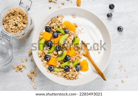 Yogurt with Granola, Kiwi, Blueberries, and Orange in a Bowl, Healthy Snack or Breakfast on Bright Background