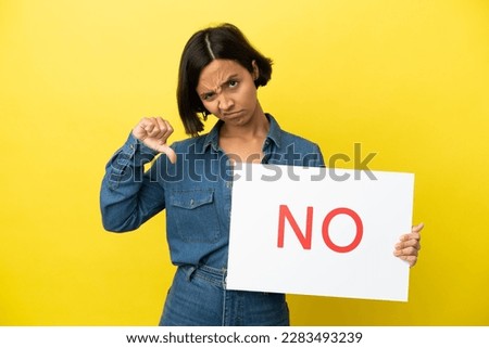 Young mixed race woman isolated on yellow background holding a placard with text NO