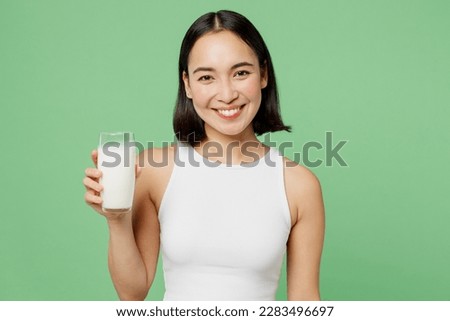 Young smiling happy fun woman wear white clothes hold in hand glass drink milk look camera isolated on plain pastel light green background. Proper nutrition healthy fast food unhealthy choice concept Royalty-Free Stock Photo #2283496697