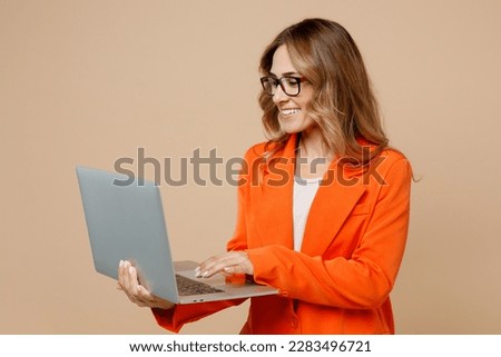 Young confident happy employee IT business woman corporate lawyer 30s wearing classic formal orange suit glasses work in office hold use laptop pc computer isolated on plain beige background studio