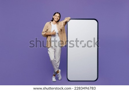 Full body smiling young latin woman wear light shirt casual clothes big huge blank screen mobile cell phone smartphone with area show thumb up isolated on plain pastel purple color background studio