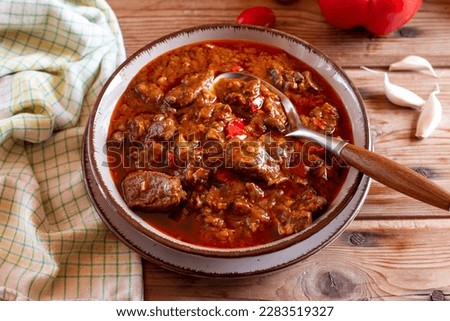 Pork goulash meat with dumplings on plate, cutlery, garlic, onion, tablecloth in the background - typical Czech food Royalty-Free Stock Photo #2283519327