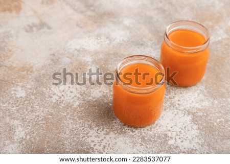 Baby puree with fruits mix, pumpkin, persimmon, mango infant formula in glass jar on brown concrete background. Side view, copy space, artificial feeding concept.
