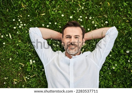 Handsome adult man lying down on grass with daisies  Royalty-Free Stock Photo #2283537711