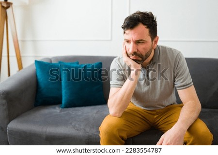 Sad depressed caucasian man feeling lonely and upset while thinking about his problems sitting on the sofa at home Royalty-Free Stock Photo #2283554787