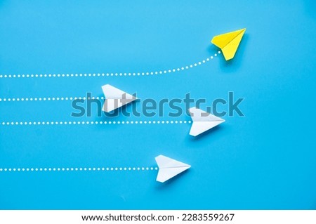 Top view of paper airplane - Yellow paper airplane origami flying to a different direction leaving other white airplanes on blue background