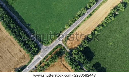 Automobile asphalt road with cars driving along it between agricultural fields with yellow ripened wheat and different green agricultural crops. Aerial drone view. Agricultural agrarian crop landscape