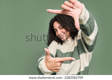 Young happy positive pretty latin woman having fun isolated on green background. Smiling female model pretending holding camera in hands and talking photo shot standing at color wall.