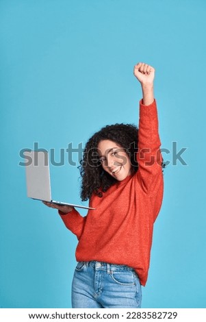 Young happy latin woman winner holding laptop isolated on blue background. Excited lucky female student using computer winning online celebrating success admission with yes gesture concept. Royalty-Free Stock Photo #2283582729