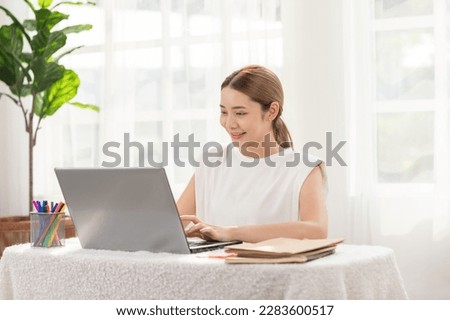 Modern and successful Asian woman working on her laptop with a bright smile. Embodies productivity, efficiency, Balance between work and happiness. For promoting career advancement and technology