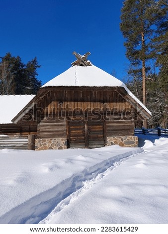 Old wooden house under a thatched roof on a sunny winter day. Path in the snow leading to the house. Royalty-Free Stock Photo #2283615429
