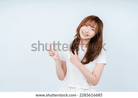 Young confident woman showing logo on empty space. Smiling girl inviting or advertising promo deal, pointing fingers left and looking at camera, white background. Royalty-Free Stock Photo #2283616685