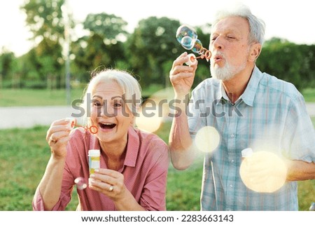 Happy active senior couple having fun blowing soap bubbles in park outdoors. Vitality and active senior couple concept Royalty-Free Stock Photo #2283663143