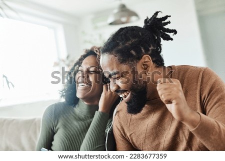 Portrait of a lovely young couple having fun and listening music wearing earphones and holding tablet together at home Royalty-Free Stock Photo #2283677359