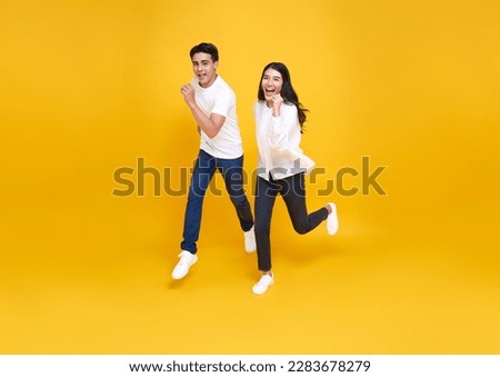 Happy energetic Asian couple running to shopping black friday low prices summer sale isolated on yellow studio background.