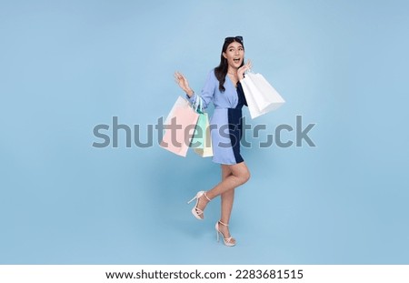 Beautiful fashionable Asian woman holding shopping bags looking to copy space Wow and surprised sale concept isolated on blue studio background. Royalty-Free Stock Photo #2283681515
