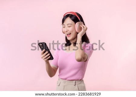 Portrait young cheerful asian woman enjoy listening audio by smartphone music application against pink. Happy smiling female person with headphone. Sound, leisure, lifestyle, technology concept Royalty-Free Stock Photo #2283681929