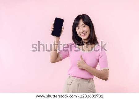 Portrait beautiful young asian woman happy smile showing smartphone screen with pointing finger hand gesture to mobile phone isolated on pink pastel studio background.