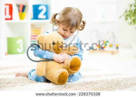 Cute kid girl playing doctor with plush toy at home Royalty-Free Stock Photo #228370108