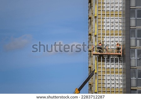 Workers sheathe the outer walls of a brick house with insulation. Insulation of the facade of the building. The concept of exterior decoration, moisture protection, sound insulation, energy saving. Royalty-Free Stock Photo #2283712287