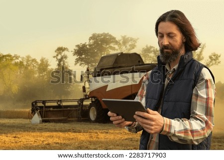 Farmer with digital tablet on a background of harvester. Smart farming concept.