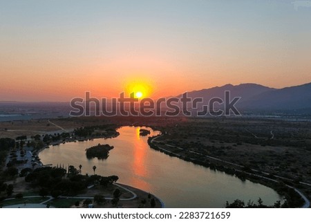 a shot of the rippling waters of the Santa Fe Reservoir with a stunning orange sunset with lush green trees and majestic mountain ranges at Santa Fe Dam Recreation Area in Irwindale California