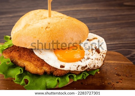 Tasty schnitzel sandwich with sunny side up egg served on cutting board 