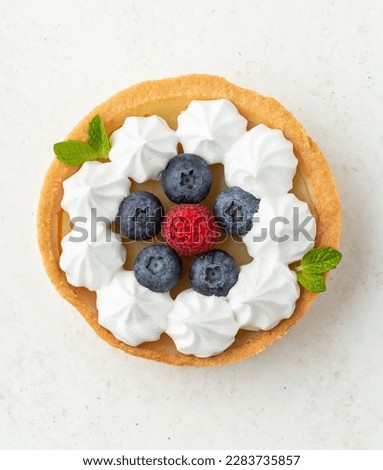 Overhead shot of a lemon meringue tartlet garnished with fresh berries