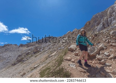 Young woman with sunglasses, long air and cap walking in the middle of dolomite peaks, Latemar, Trentino, Italy. Traveling photography and outdoor sport activity concept