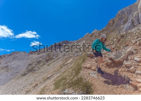 Young woman with long air and cap walking in the middle of dolomite peaks. Scenic landscape on the nature, Mount Latemar, Trentino, Italy. Traveling photography and outdoor sport activity concept