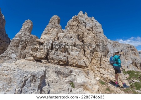 Girl with long air and cap taking photos with phone of dolomite peaks. Scenic landscape on the nature, Mount Latemar, Trentino, Italy. Traveling photography and outdoor sport activity concept