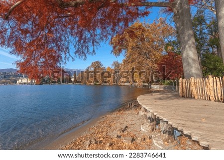 Colorful autumn colored trees on the shore of Lugano lake over wooden footbridge, Switzerland. Concept about tranquility and relaxation