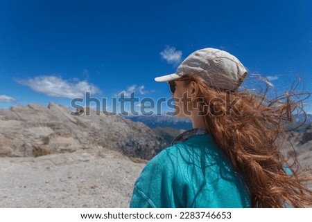 Portrait from behind of young woman in sunglasses with hair blowing in the wind who is hiking outdoors in mountains, Latemar, Trentino, Italy. Traveling concept photography and outdoor sport activity