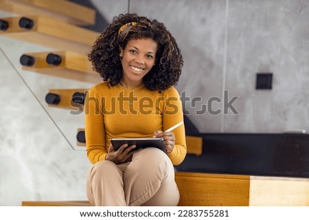 Portrait of female designer working in modern office.Smiling african-american businesswoman using digital tablet in office.She is looking at camera.
