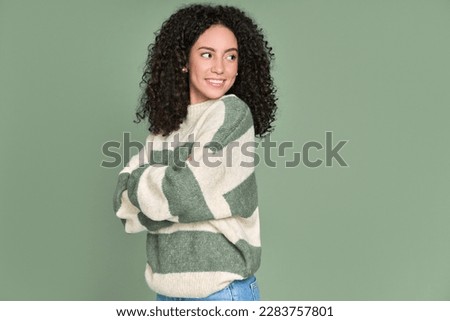 Young happy latin woman looking aside at copy space isolated on green background. Smiling female model curious about new sale offer presenting promotion commercial ad discounts concept.