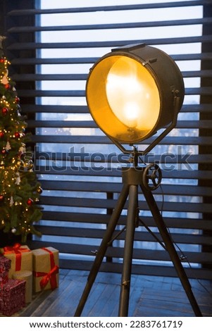Old video lamp light on a tripod in the interior. Lamp on the background of a window with blinds. Dark blinds in the interior.