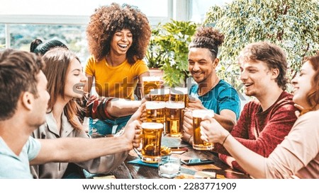 Multiracial friends toasting beer glasses at brewery pub garden - Happy young people enjoying happy hour sitting at bar restaurant - Friendship concept with guys and girls drinking and eating together
