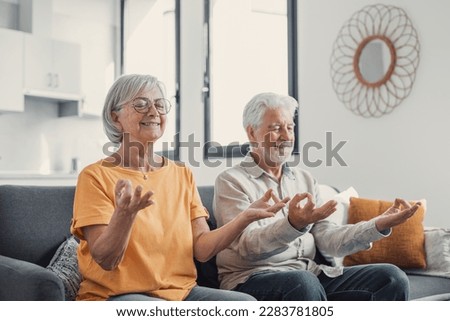 Calm senior middle aged couple practicing yoga together sitting in lotus pose on sofa, mindful peaceful mature man and woman meditating relaxing in living room at home, old people healthy lifestyle Royalty-Free Stock Photo #2283781805