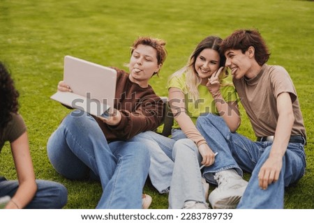 Young students having fun together taking a selfie with digital tablet while sitting outside of university meadow Royalty-Free Stock Photo #2283789739