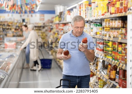 Focused aged man reading labels on bottles with sauces in supermarket, carefully examining ingredients and expiration date while shopping for groceries Royalty-Free Stock Photo #2283791405