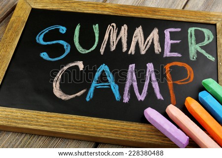 Text Summer camp written with chalk on chalkboard, and some chalk sticks of different colors